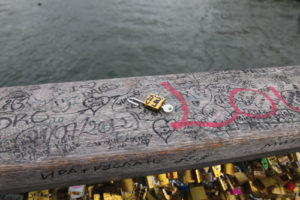 A footbridge in Paris over the Seine River and its fencing is covered with padlocks affixed by couples.